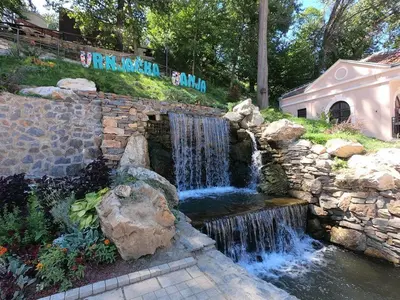 a waterfall in a garden with a stone wall at Centar Park Lux in Vrnjačka Banja