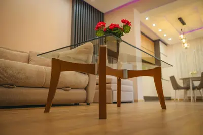 a glass table with a vase of red flowers on it at Apartman Dias in Niš