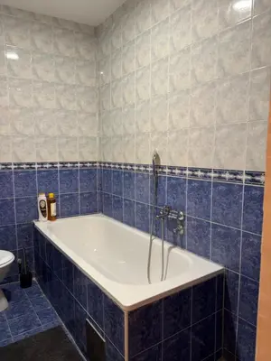 a blue tiled bathroom with a tub and a toilet at Loli apartman 2 in Kraljevo