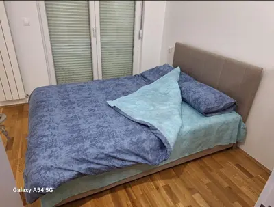 a bed with blue blankets and pillows on a wooden floor at Apartman Centrala in Pirot