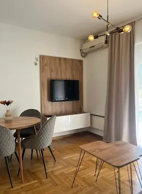 a living room with a table and a television on a wall at Apartman Anja in Vrnjačka Banja
