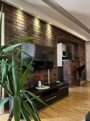 a living room with a tv and a brick wall at Delux apartman in Leskovac