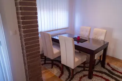 a dining room table with white chairs and a brick wall at Apartmani Stanković in Vranje