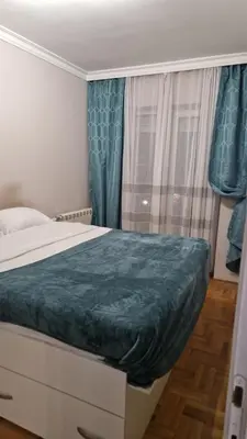 a bedroom with a bed and a window with blue curtains at JM Apartman in Donja Vrežina