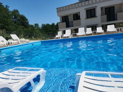 a swimming pool with white chairs and a building at Apartman Nika Vb in Vrnjačka Banja