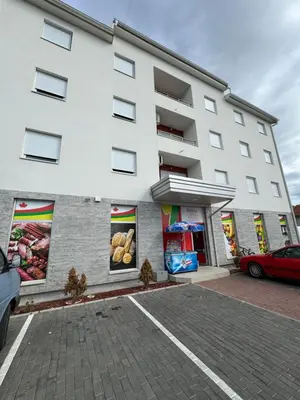 a white building with a car parked in a parking lot at Brasic Apartman in Zaječar