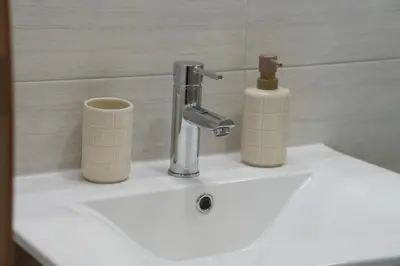 a bathroom sink with a faucet and two cups on it at NOVA Apartmani in Kraljevo