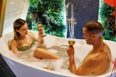 a man and woman in a bath tub with glasses of wine at Luxurious cabin for couples with hot tub lake view in Aleksinac