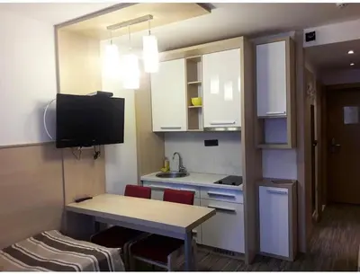 a small kitchen with white cabinets and a table and a television at Konaci Angella apartman 126 in Kopaonik
