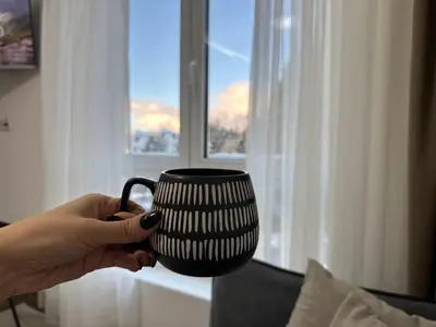 a person holding a black mug in front of a window at Milanovic Apartman in Kopaonik