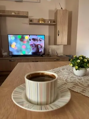 a cup of coffee sitting on a table with a television at Apartman KVINS in Kruševac