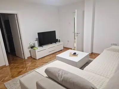 a white living room with a couch and a tv at Apartman Leskovac in Leskovac