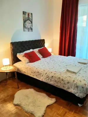 a bedroom with a bed with red pillows and a rug at Apartman Trijumf in Vrnjačka Banja