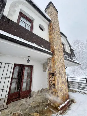 a house with a stone chimney in the snow at Vila Aurora , 50m od Gondole Brzece in Brzeće