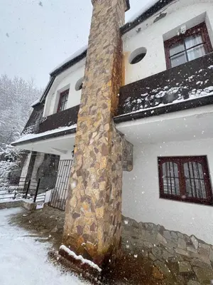 a house with a stone chimney in the snow at Vila Aurora , 50m od Gondole Brzece in Brzeće