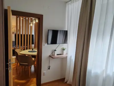 a room with a table and a television and a door at Brzece lux apartman in Brzeće