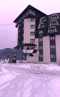 a building in the snow in front of a street at Sunčana planina apartman 104 in Kopaonik