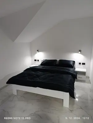 a white bedroom with a black bed with two lights at Garfield Family Apartman 2 in Soko Banja
