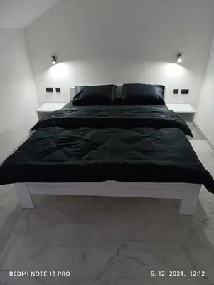 a white bedroom with a bed with a black comforter at Garfield Family Apartman 2 in Soko Banja