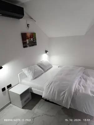 a bedroom with a white bed with a night stand at Garfield Family Studio 1 in Soko Banja