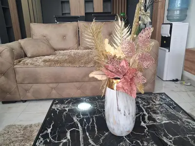a vase with flowers on a table in front of a couch at Dina lux apartman 2 in Jagodina