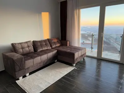 a living room with a brown couch and a large window at Vila Banovic in Kopaonik
