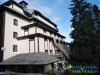 a large white building with a tree in front of it at Apartman Sivi Vuk Kopaonik in Kopaonik