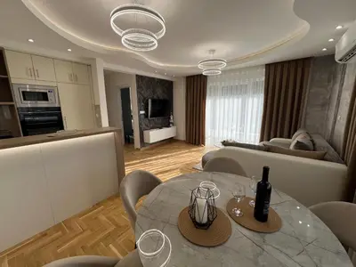 a kitchen and a living room with a table with wine glasses at Apartman Lux Jocić in Vrnjačka Banja