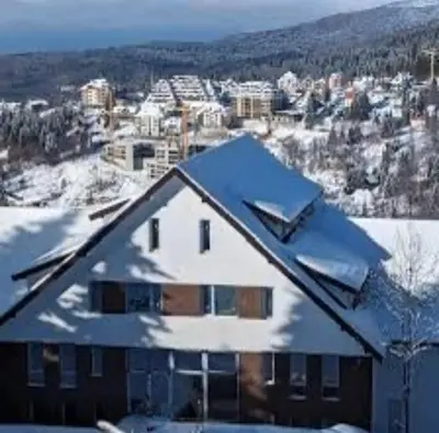 a house covered in snow with a city in the background at Apartment Treska Kop in Kopaonik