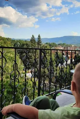 a man and a woman sitting on a balcony looking out at the mountains at Apartmani Vila Dragana Vrnjačka Banja in Vrnjci