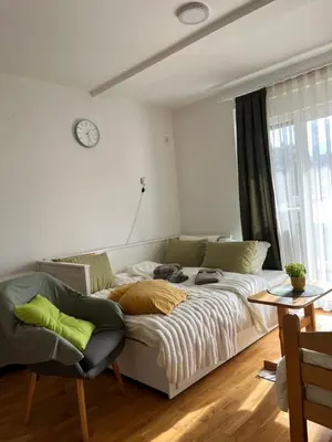 a white couch in a living room with a clock on the wall at Apartman Green in Vrnjačka Banja