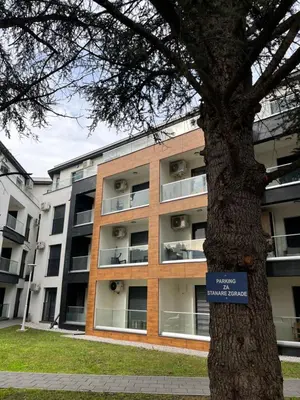 an apartment building with a sign in front of a tree at Apartman Green in Vrnjačka Banja