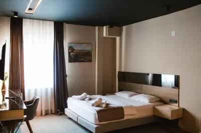 a bedroom with a bed and a desk and a window at Garni Uni Elita Lux Hotel in Niš