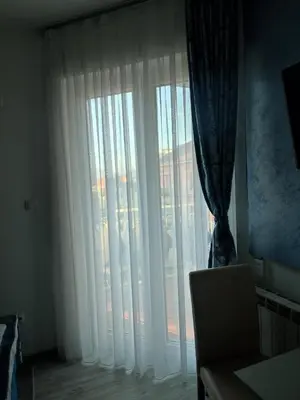 a room with a window with white curtains and a chair at Apartman Plava nota in Vrnjačka Banja