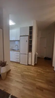 a kitchen with a white refrigerator and a wooden floor at Konatar Apartmants in Kruševac