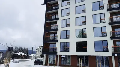 a white building with black windows on a snowy street at Tontic Lux Residence Hill 54 in Kopaonik