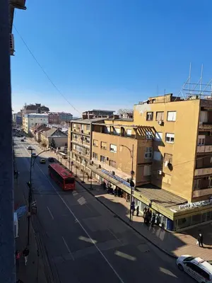 a city street with buildings and a red bus at Apartman Tea in Niš