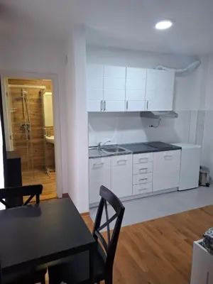a kitchen with white cabinets and a table and a dining room at Apartman STAR Vrnjačka Banja in Vrnjci