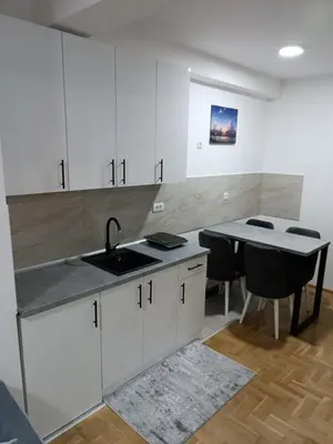 a kitchen with white cabinets and a sink and a table at Apartman David in Vrnjci
