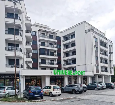 a large white building with cars parked in a parking lot at Apartman David in Vrnjci