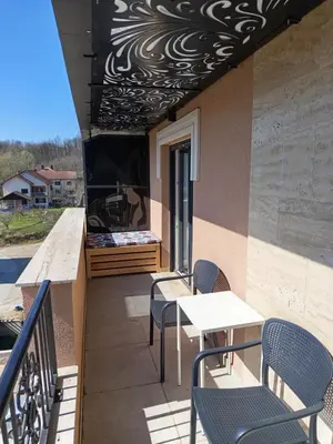 a balcony with chairs and a table and a tv at Ramonda apartman sa bazenom, Vrnjačka Banja in Vrnjačka Banja