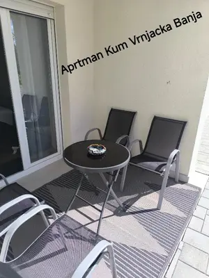 a table and chairs on a patio with a sign on the wall at Apartman KUM in Vrnjačka Banja