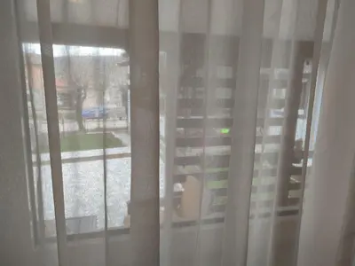 a window with white curtains and a view of a yard at Miris Proleća in Rekovac