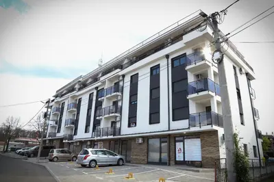 a white building with cars parked in a parking lot at Apartman Aleksandra Vrnjacka Banja in Vrnjci