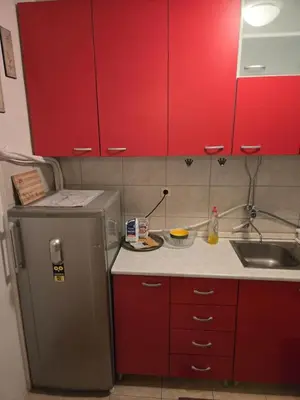 a small kitchen with red cabinets and a refrigerator at Apartman u Nisu in Niš