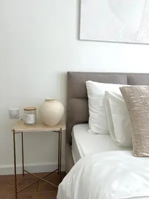 a bed with white pillows and a vase on a side table at Japandi Home in Niš