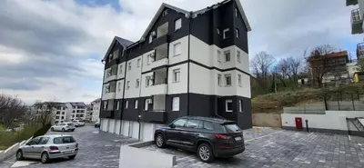 a black and white building with cars parked in a parking lot at Apartman Kety Sokobanja in Soko Banja