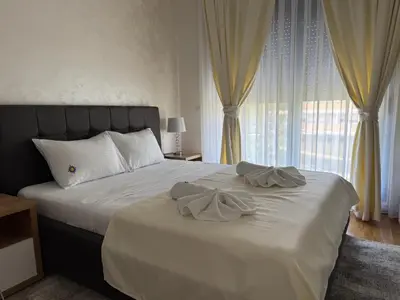 a bedroom with a bed with white sheets and curtains at Apartman Sunce Lux A in Vrnjačka Banja