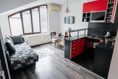 a kitchen with red cabinets and a couch in a room at Apartman Maja in Niš