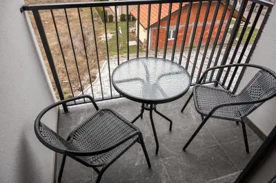 a glass table and three chairs on a balcony at Toplina Doma Sokobanja in Soko Banja